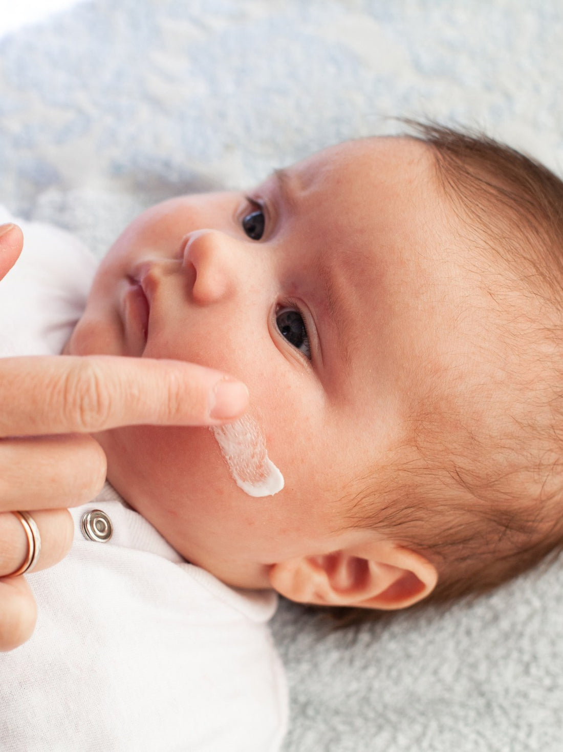 Parent gently applying moisturising cream to a baby's cheek