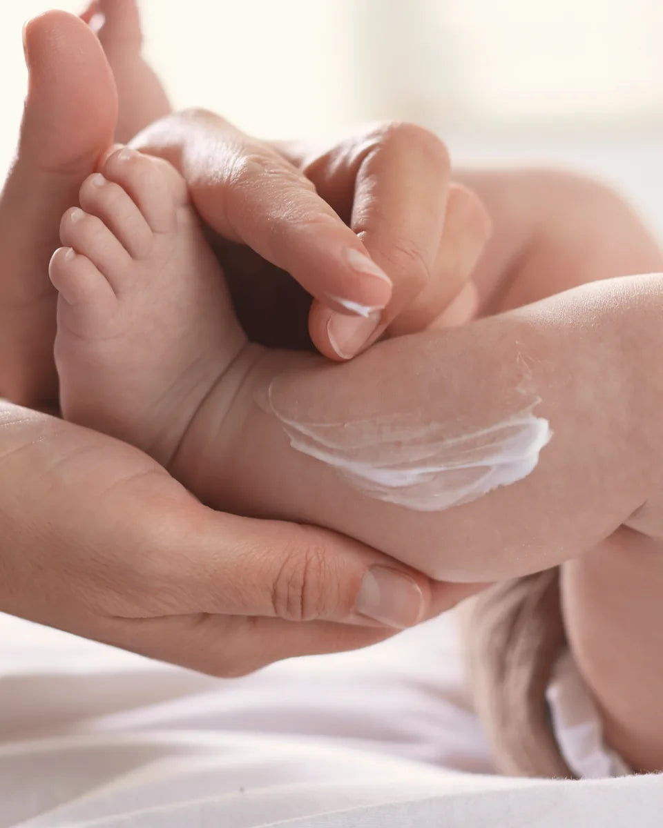 A parent's hands smoothing cream onto a baby's leg